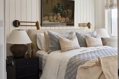 a bed with white linens and pillows in a bedroom next to a painting on the wall