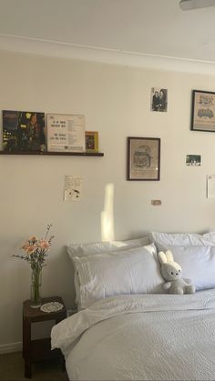 a bed with white linens and pictures on the wall above it, along with a stuffed animal