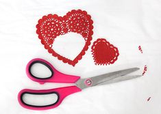 two pairs of pink scissors next to red doily