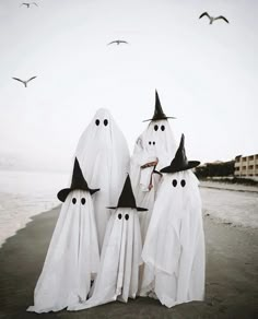 three white ghost figures standing on the beach with black hats and long cloaks over their heads