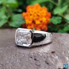 a white diamond ring sitting on top of a wooden table next to some orange flowers