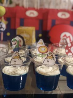 cupcakes with white frosting and cartoon characters on them are displayed in plastic cups