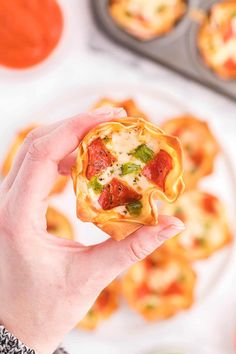 a person holding up a small pizza in front of some muffins on a plate