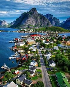 an aerial view of a small town by the water with mountains in the background and boats on the water