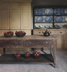 an old wooden table with bowls and plates on it in front of some cupboards