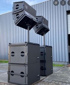 three large speakers stacked on top of each other in front of a metal building with windows