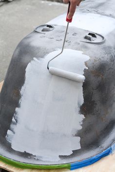 a person using a brush to paint the top of a metal object with white paint