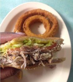 a hand holding a sandwich with onion rings on the side