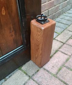 a wooden door handle next to a brown door on brick sidewalk with black frame and glass