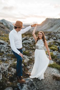 a man and woman standing on top of a rocky hillside holding hands in the air