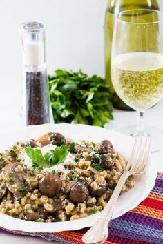 a white plate topped with pasta and mushrooms next to a glass of wine on a table