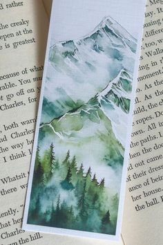 a bookmark with watercolor painting of mountains and trees on it's side