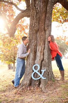 a man and woman leaning against a tree with the word & amp painted on it