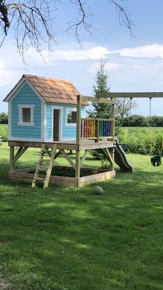 a small blue house sitting on top of a lush green field next to a playground