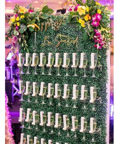 a green wall with lots of wine glasses on it and flowers hanging from the side