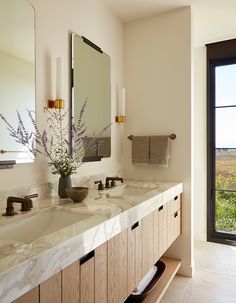 a bathroom with two sinks and mirrors in front of a large window that looks out onto the countryside