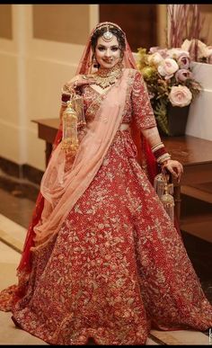 a woman in a red and gold bridal gown standing next to a flower arrangement