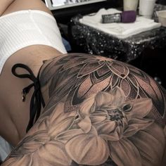 a woman's back with tattoos on it and flowers in the middle of her leg