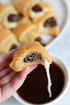 someone is holding up a pastry with chocolate filling in front of some dipping sauces