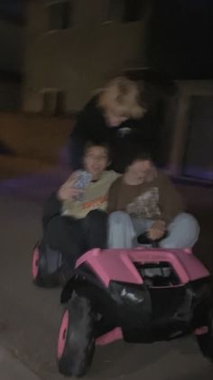 three children are riding on a pink toy car