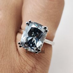 a woman's hand holding a ring with a large blue diamond in it and the center stone is surrounded by black diamonds