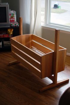 a wooden baby crib sitting on top of a hard wood floor next to a window