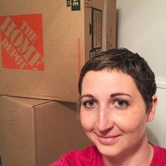 a woman in a red shirt is smiling at the camera with boxes on the wall behind her