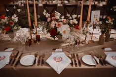 the table is set with white and red flowers, silverware, candles, and napkins