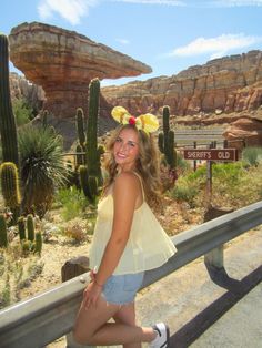 a beautiful young woman standing next to a metal fence near a desert area with cacti