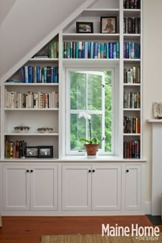 a room filled with lots of books on top of white bookcases next to a window