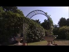 an arch in the middle of a garden with two urns on either side of it