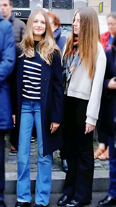 two young women standing next to each other in front of a group of people on the street