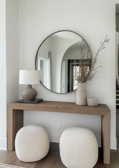 a mirror sitting on top of a wooden table next to two white poufles