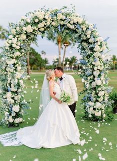 a bride and groom kissing under an arch of flowers