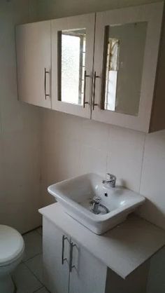 a bathroom with a toilet, sink and cabinets on the wall next to each other