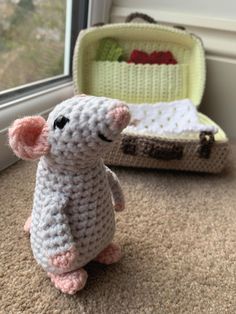 a small crocheted mouse sitting next to a suitcase on the floor in front of a window