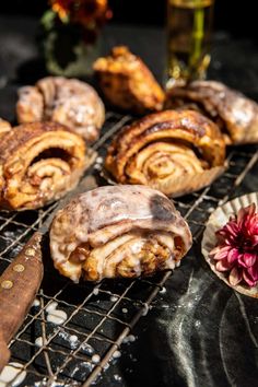 several pastries sitting on a cooling rack next to some flowers and a cutting board