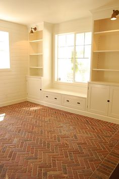 an empty room with brick flooring and built in bookshelves