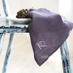 a table topped with a plate of grapes next to a purple cloth covered napkin on top of a wooden chair