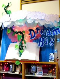 an open book on top of a shelf in front of a blue curtain with the words dream big