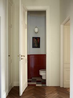 an open door leading to a bathroom with red and white walls, wood flooring