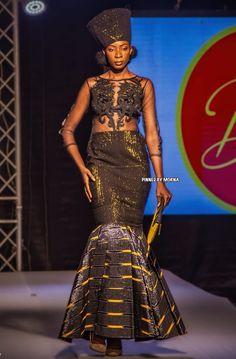 a woman in a black and gold dress on the runway at an african fashion show