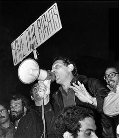 a man holding a megaphone up to his mouth while standing in front of a crowd