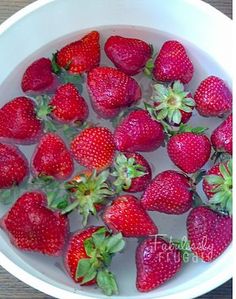 fresh strawberries are floating in water in a white bowl