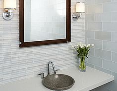 a bathroom sink sitting under a mirror next to a vase with flowers