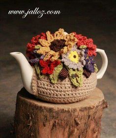 a crocheted tea pot with flowers on it sitting on top of a tree stump