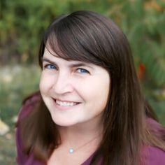 a woman with long brown hair and blue eyes smiling at the camera while wearing a purple shirt