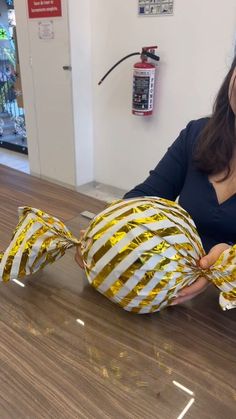 a woman sitting at a table holding two wrapped fish