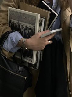 a woman is holding several books and talking on the phone while wearing a trench coat