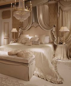 a white bed sitting under a chandelier next to two tables with lamps on them